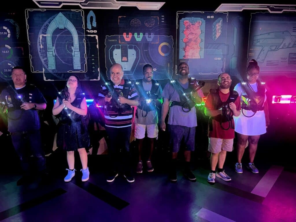 Adults standing side by side in a dark lit room wearing laser tag vests with lights.