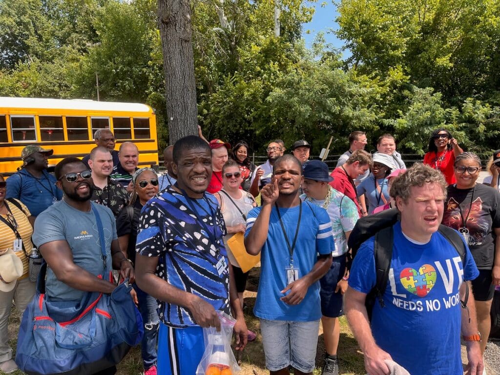 Large group of adults standing outside in front of a school bus.